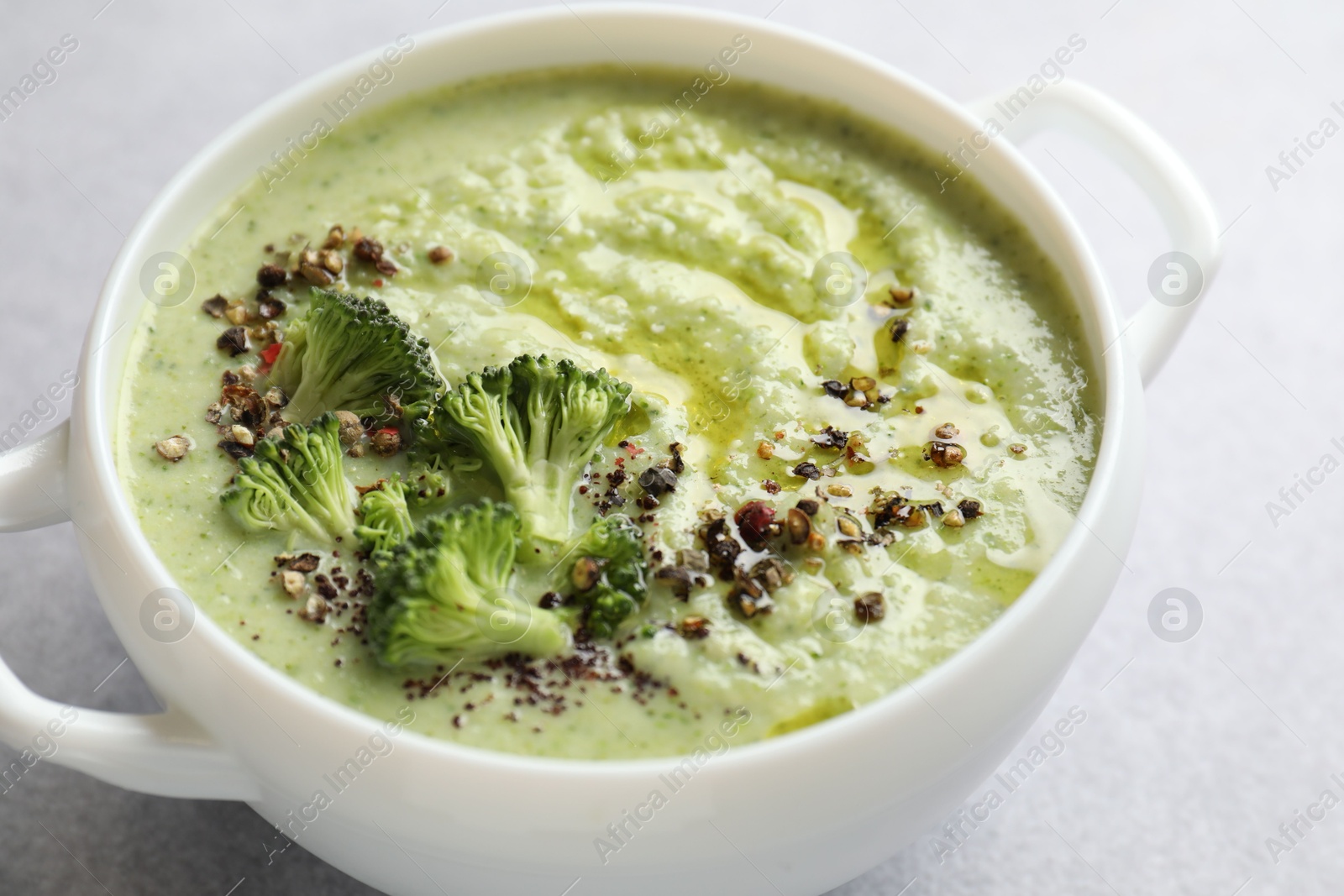 Photo of Delicious broccoli cream soup in bowl on light table, closeup