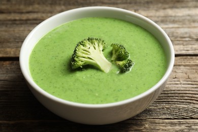 Photo of Delicious broccoli cream soup in bowl on wooden table, closeup