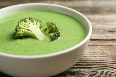 Photo of Delicious broccoli cream soup in bowl on wooden table, closeup