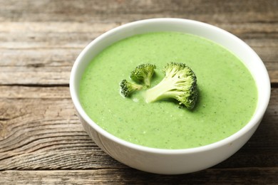 Photo of Delicious broccoli cream soup in bowl on wooden table, closeup