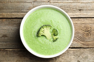 Photo of Delicious broccoli cream soup in bowl on wooden table, top view