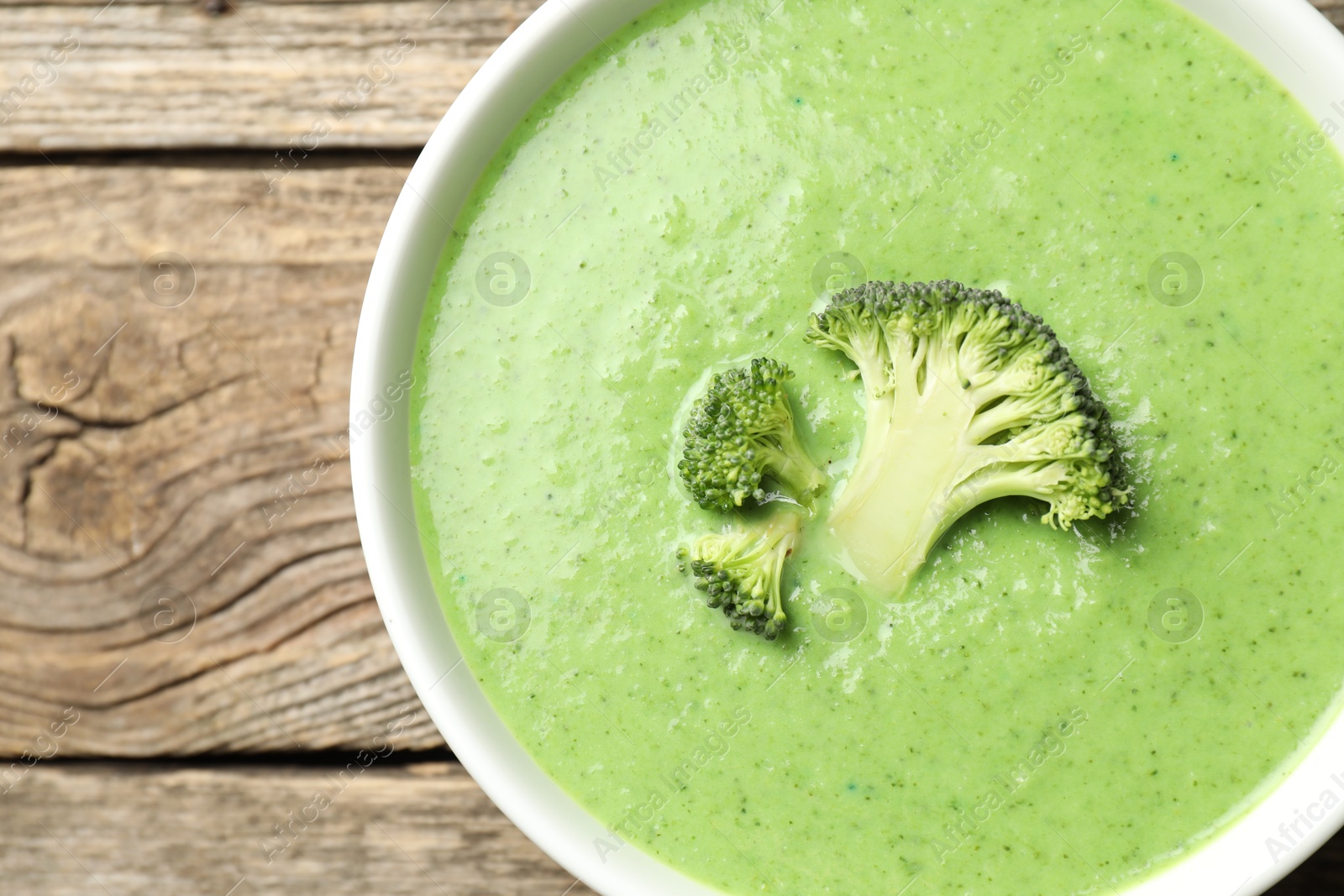 Photo of Delicious broccoli cream soup in bowl on wooden table, top view