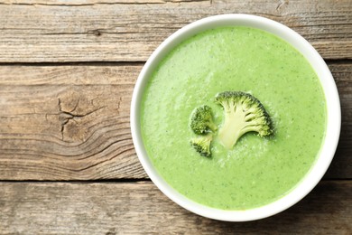 Photo of Delicious broccoli cream soup in bowl on wooden table, top view. Space for text