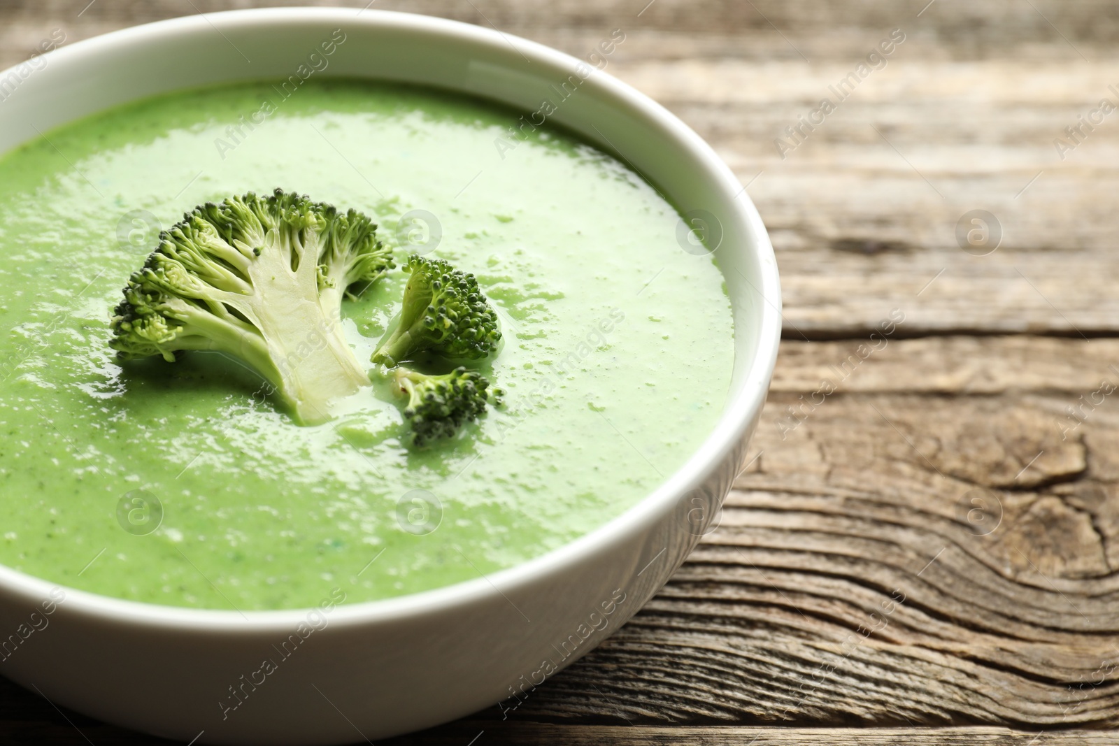 Photo of Delicious broccoli cream soup in bowl on wooden table, closeup