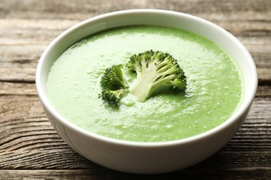 Photo of Delicious broccoli cream soup in bowl on wooden table, closeup