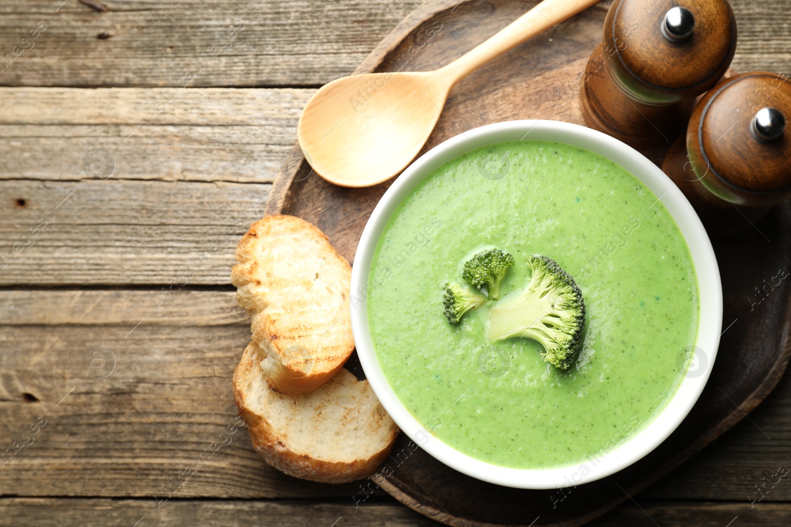 Photo of Delicious broccoli cream soup served on wooden table, top view. Space for text