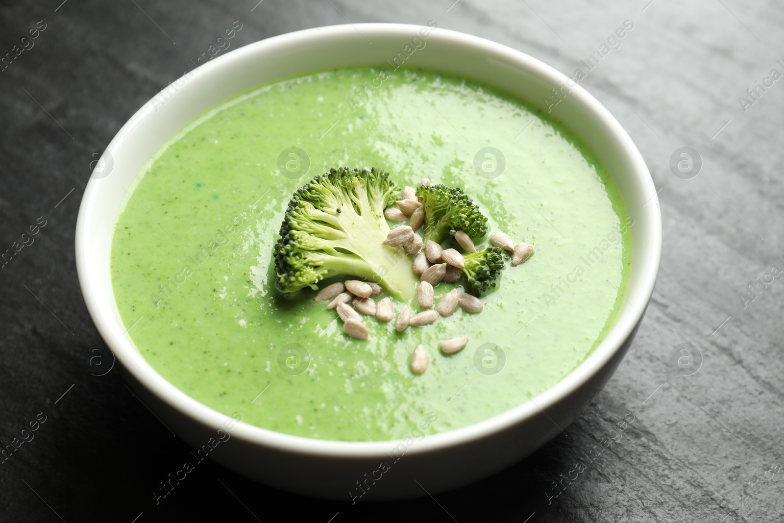 Photo of Delicious broccoli cream soup in bowl on black table, closeup