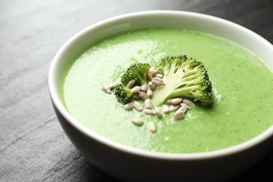 Photo of Delicious broccoli cream soup in bowl on black table, closeup