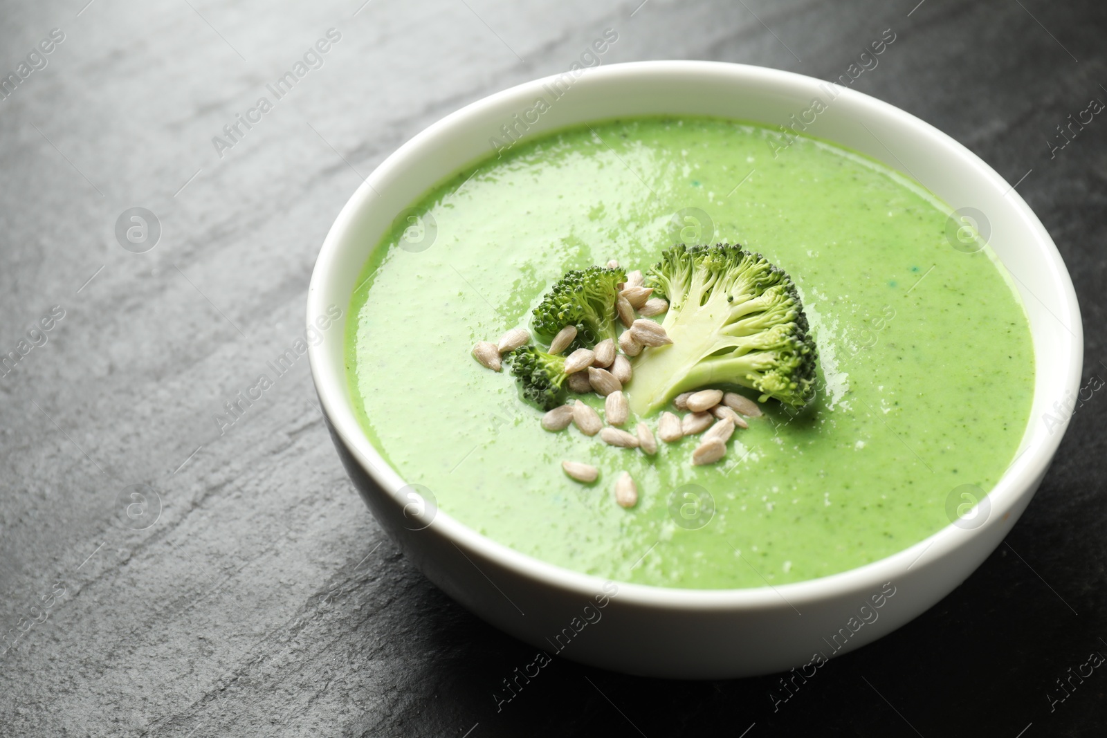 Photo of Delicious broccoli cream soup in bowl on black table, closeup