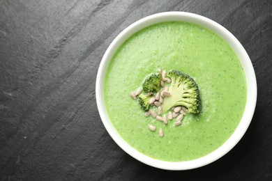 Photo of Delicious broccoli cream soup in bowl on black table, top view. Space for text