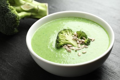 Photo of Delicious broccoli cream soup in bowl on black table, closeup