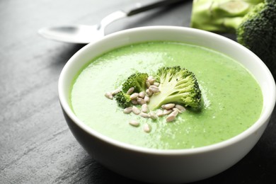 Photo of Delicious broccoli cream soup in bowl on black table, closeup