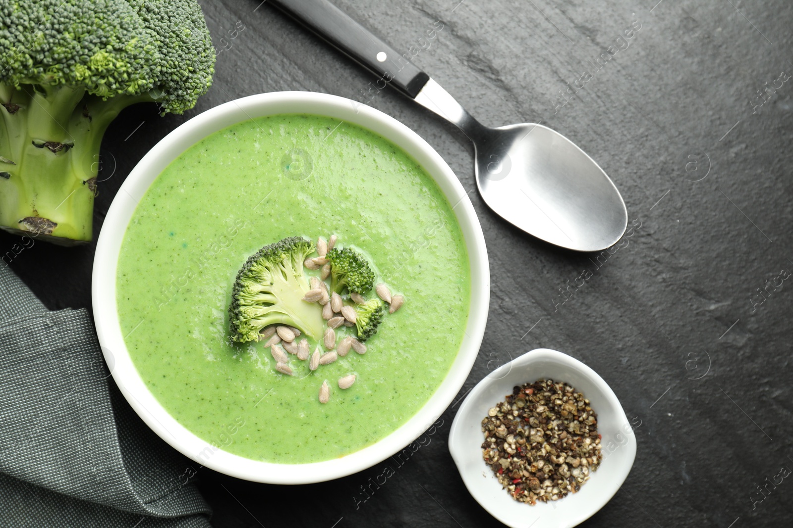 Photo of Delicious broccoli cream soup served on black table, flat lay