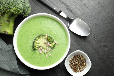 Photo of Delicious broccoli cream soup served on black table, flat lay