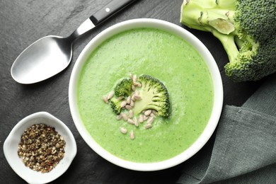 Photo of Delicious broccoli cream soup served on black table, flat lay