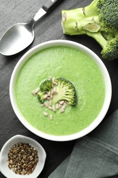 Photo of Delicious broccoli cream soup served on black table, flat lay