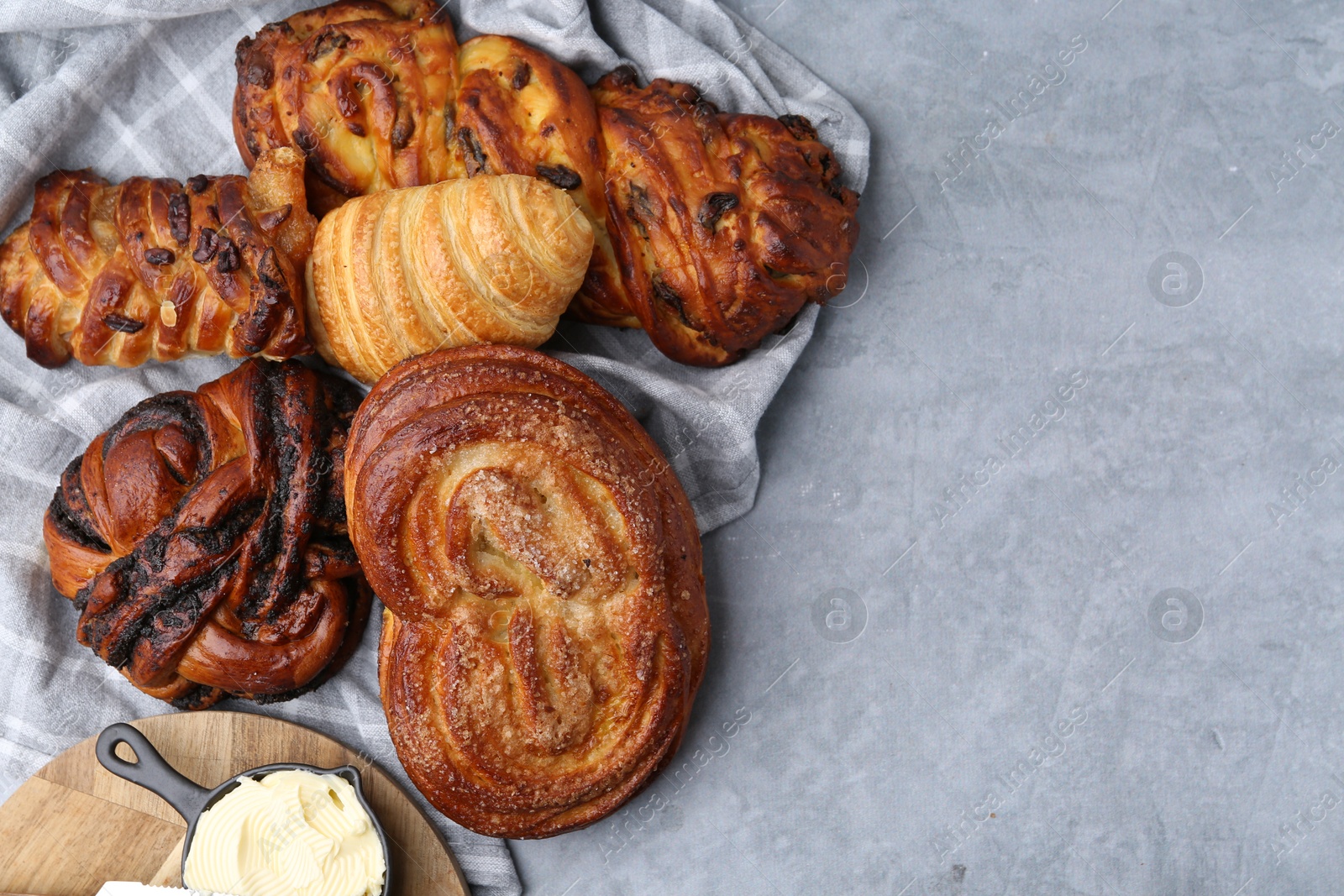 Photo of Different delicious pastries and butter on grey table, top view. Space for text