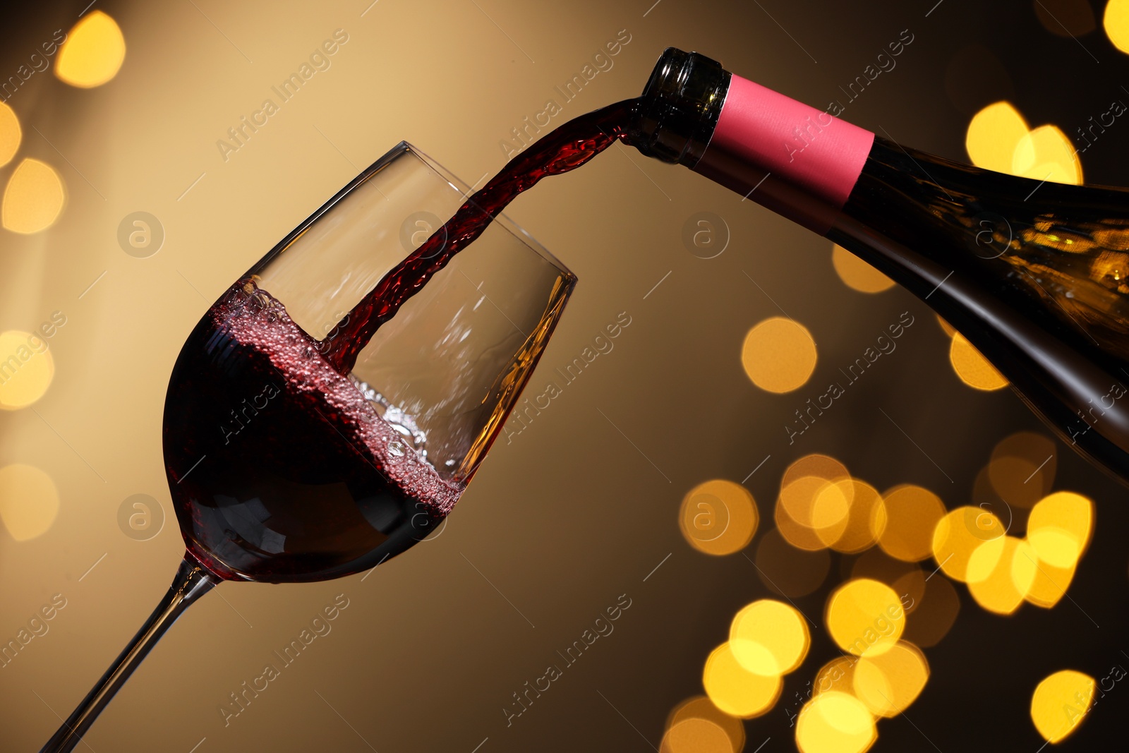 Photo of Pouring red wine into glass against beige background, closeup. Bokeh effect