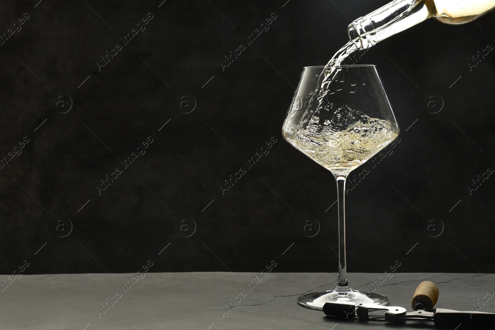 Photo of Pouring white wine into glass at grey table, space for text