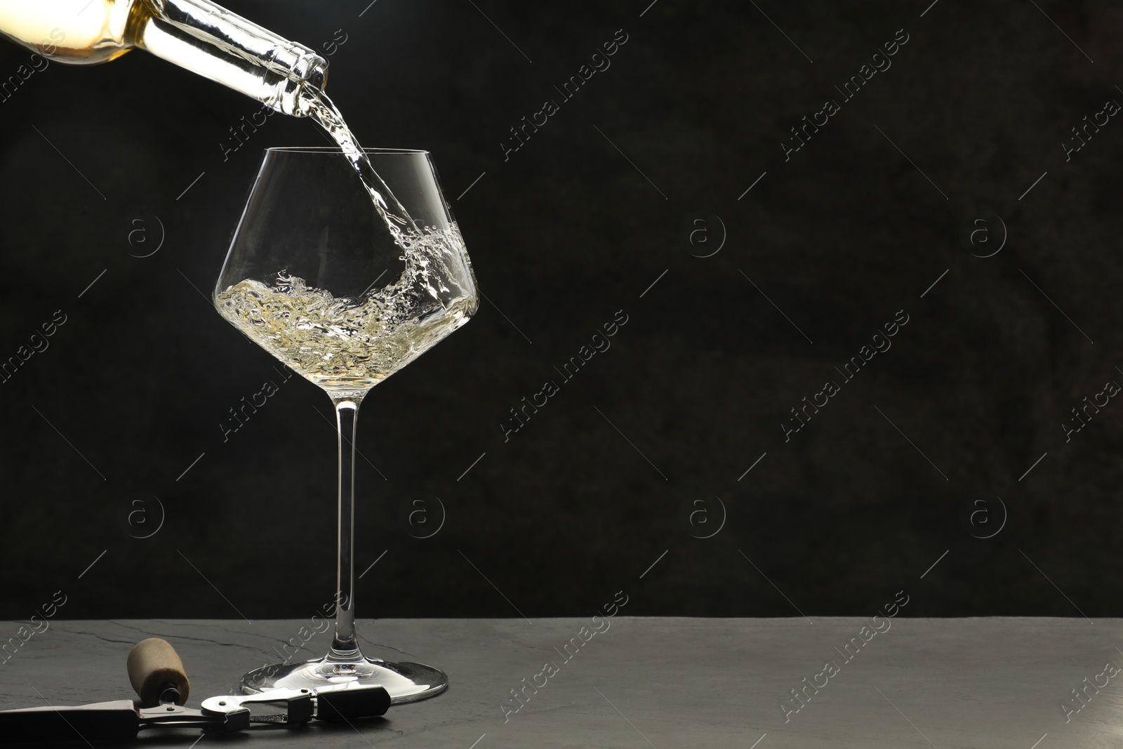 Photo of Pouring white wine into glass at grey table, space for text