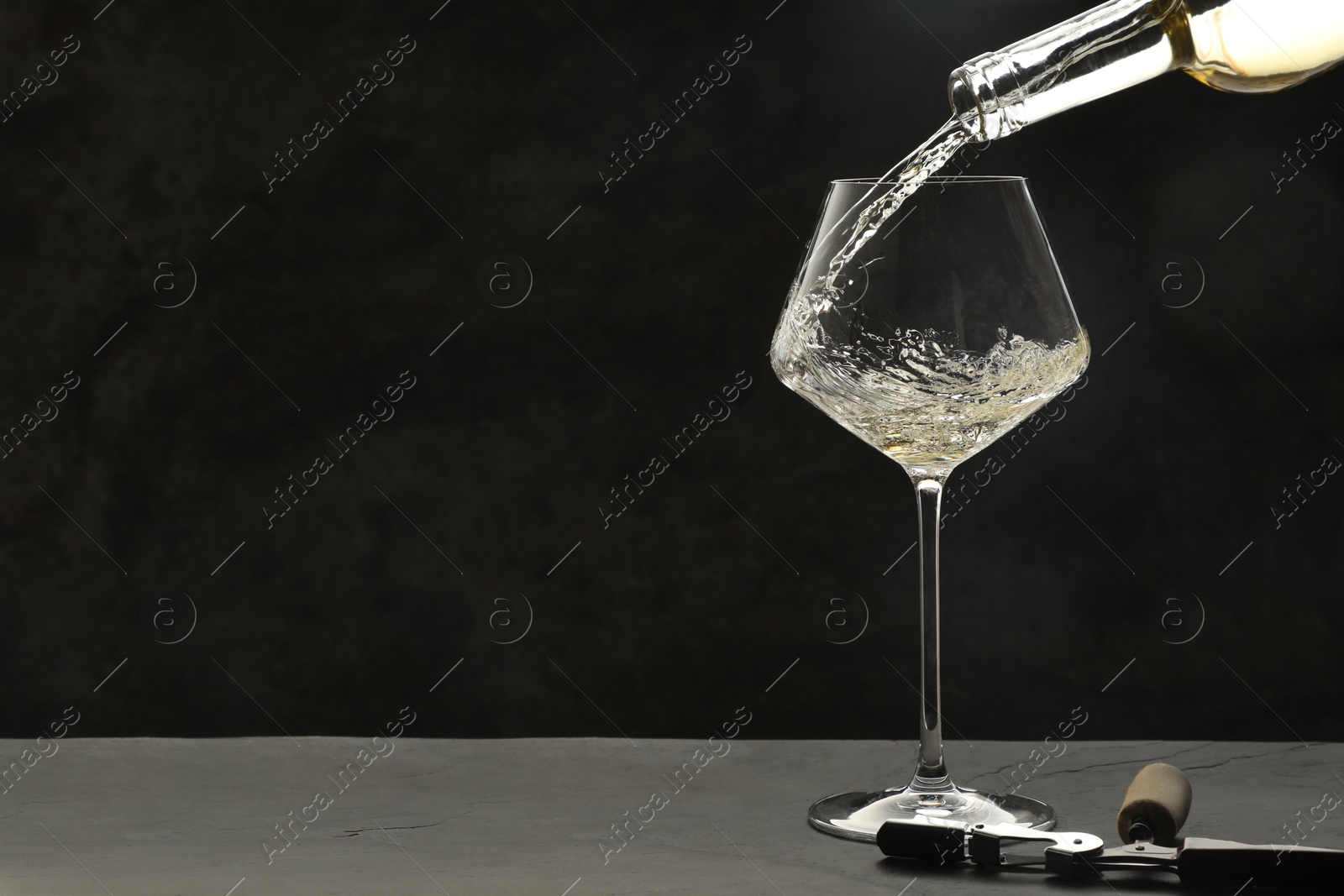 Photo of Pouring white wine into glass at grey table, space for text