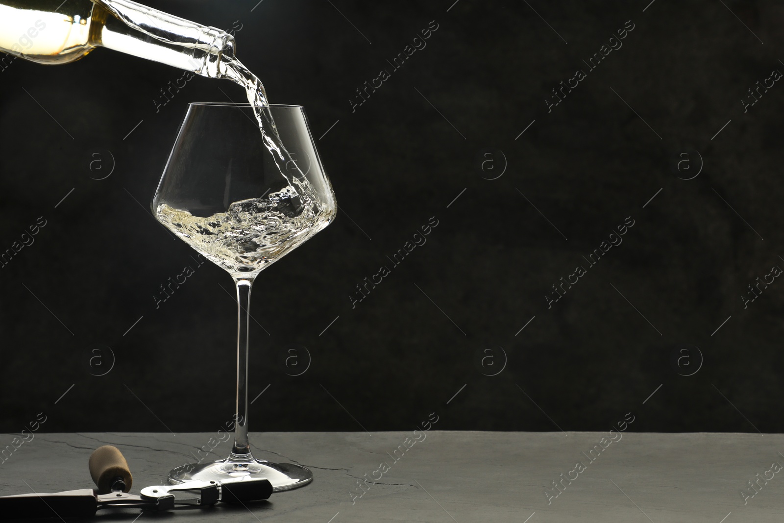 Photo of Pouring white wine into glass at grey table, space for text