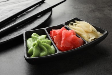 Photo of Hot wasabi paste, ginger and chopsticks on grey table, closeup