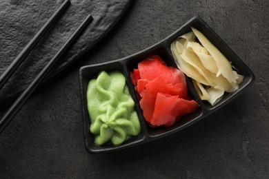 Photo of Hot wasabi paste, ginger and chopsticks on grey table, top view