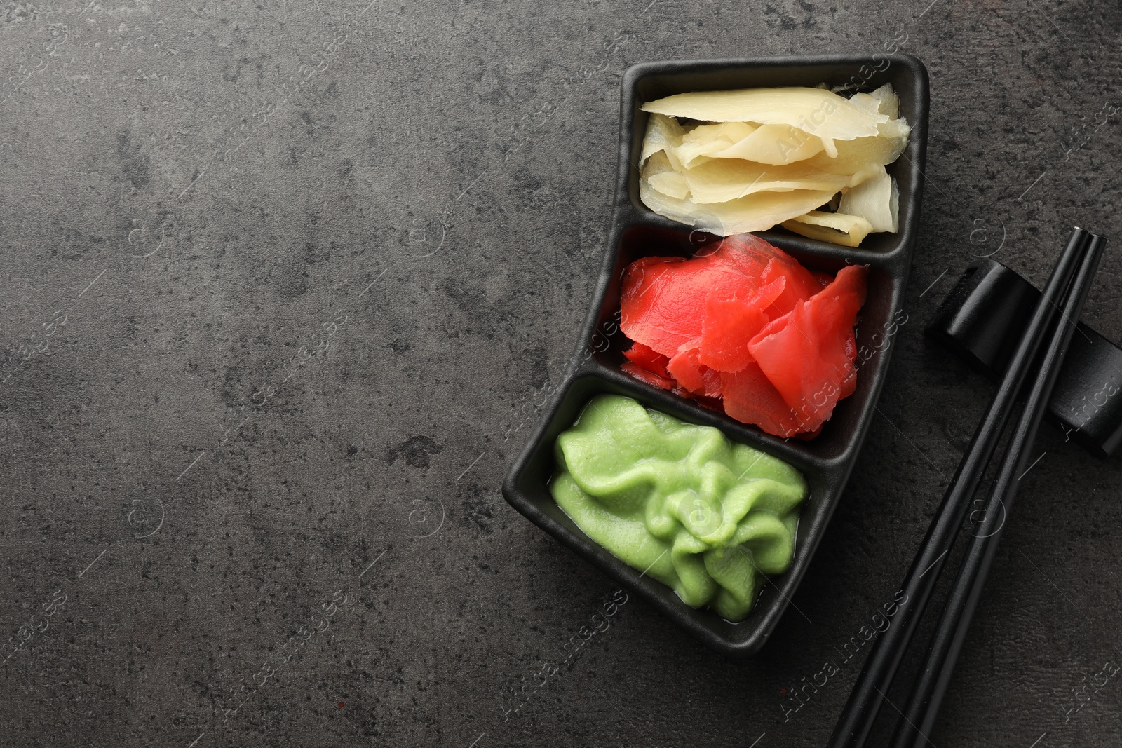 Photo of Hot wasabi paste, ginger and chopsticks on grey table, top view. Space for text