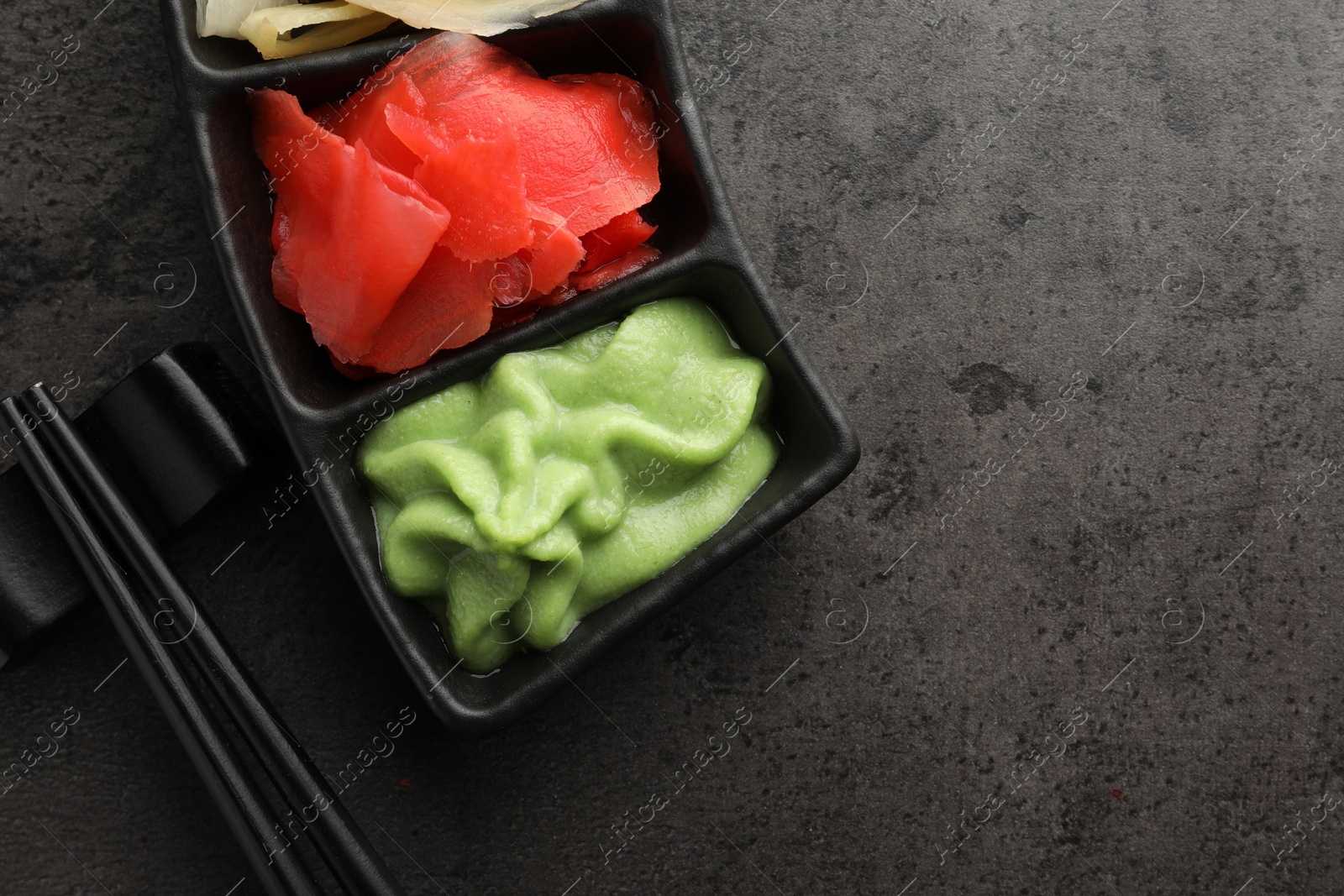 Photo of Hot wasabi paste, ginger and chopsticks on grey table, top view. Space for text