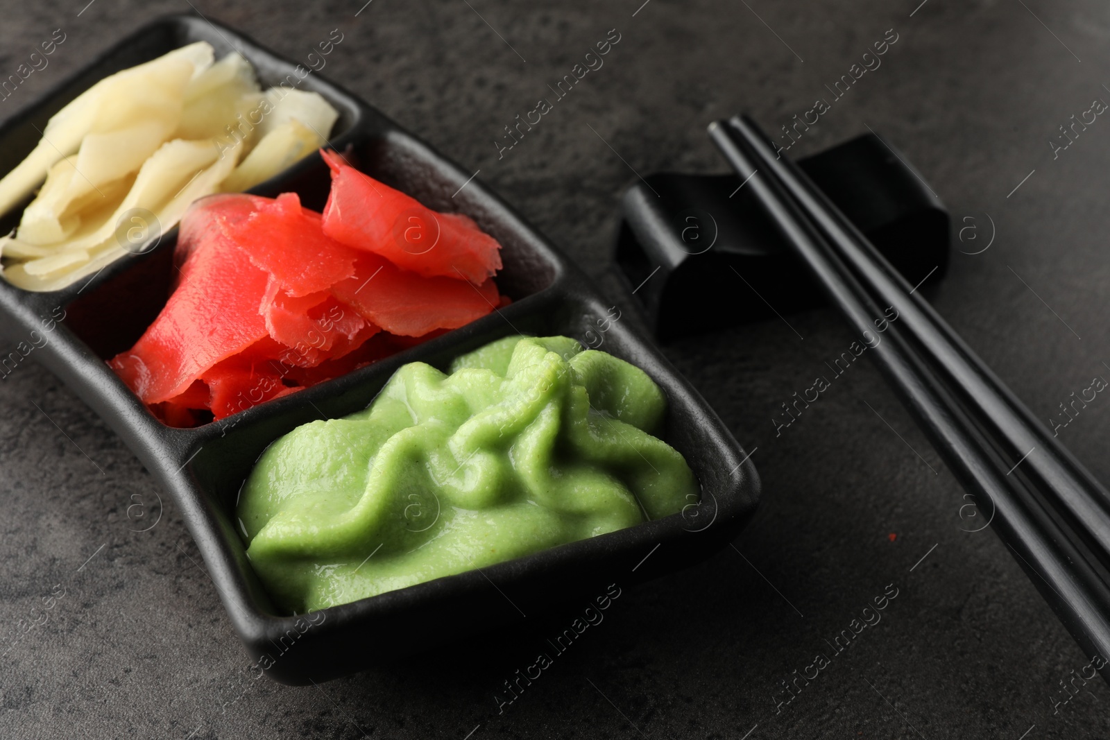 Photo of Hot wasabi paste, ginger and chopsticks on grey table, closeup