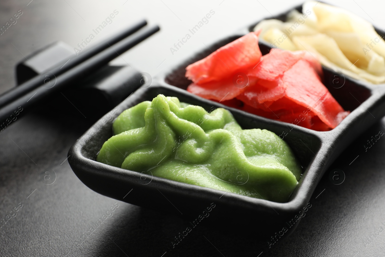 Photo of Hot wasabi paste, ginger and chopsticks on grey table, closeup