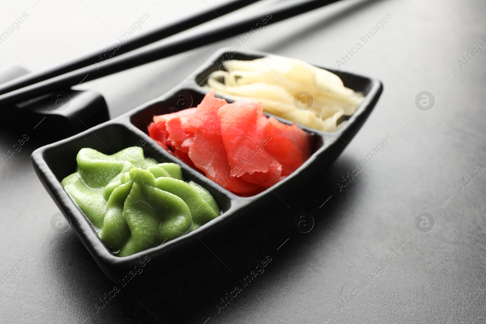 Photo of Hot wasabi paste, ginger and chopsticks on grey table, closeup