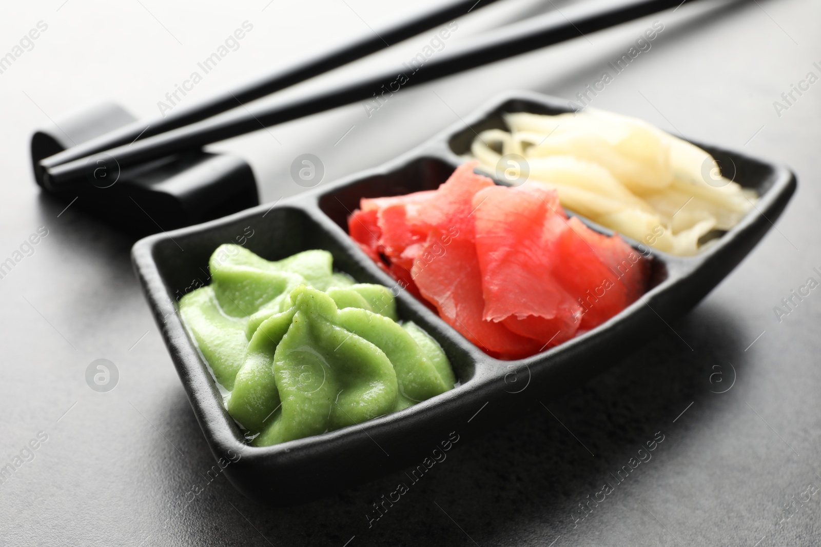 Photo of Hot wasabi paste, ginger and chopsticks on grey table, closeup