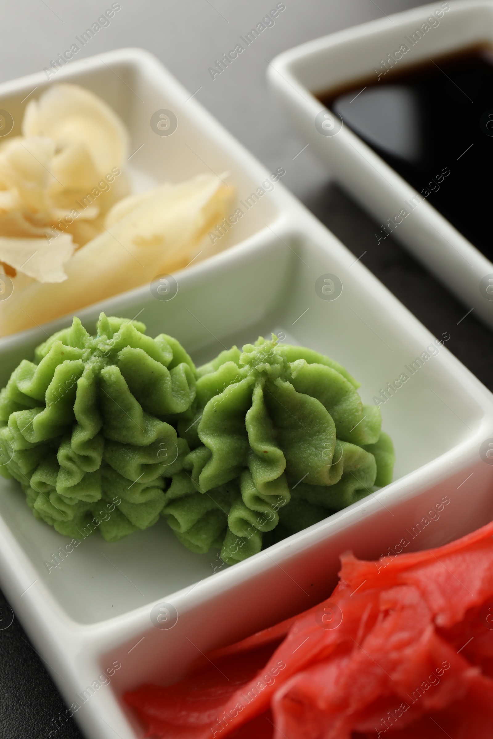 Photo of Hot wasabi paste, ginger and soy sauce on grey table, closeup