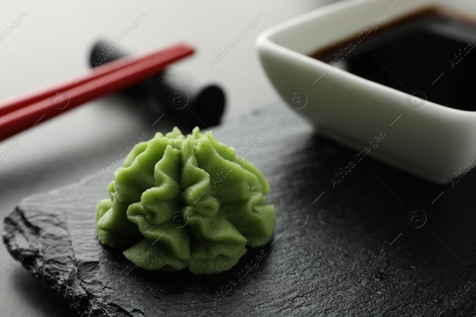 Photo of Hot wasabi paste, soy sauce and chopsticks on grey table, closeup