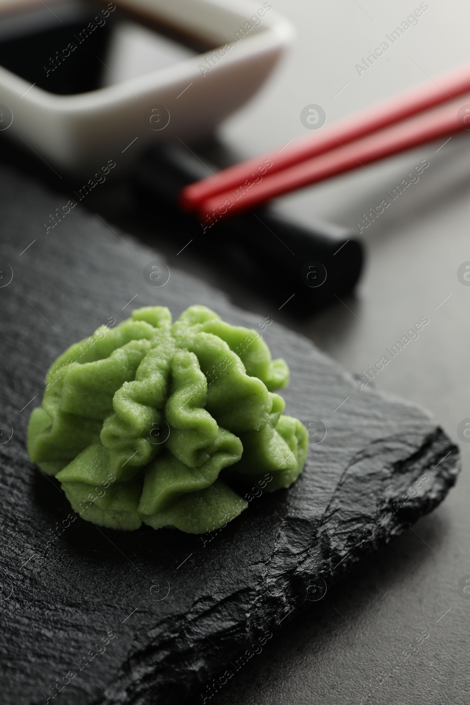 Photo of Hot wasabi paste, soy sauce and chopsticks on grey table, closeup