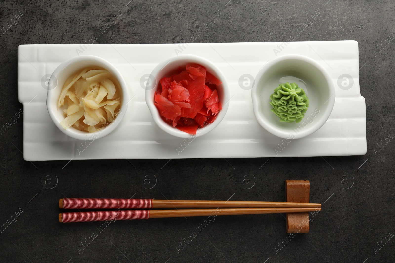 Photo of Hot wasabi paste, ginger and chopsticks on grey table, top view