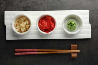 Photo of Hot wasabi paste, ginger and chopsticks on grey table, top view