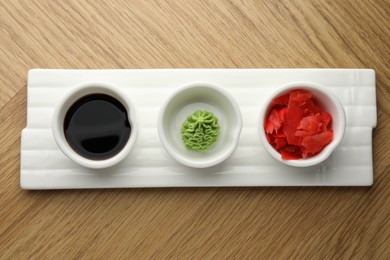 Photo of Hot wasabi paste, soy sauce and ginger on wooden table, top view