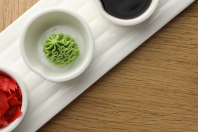 Photo of Hot wasabi paste, soy sauce and ginger on wooden table, top view. Space for text