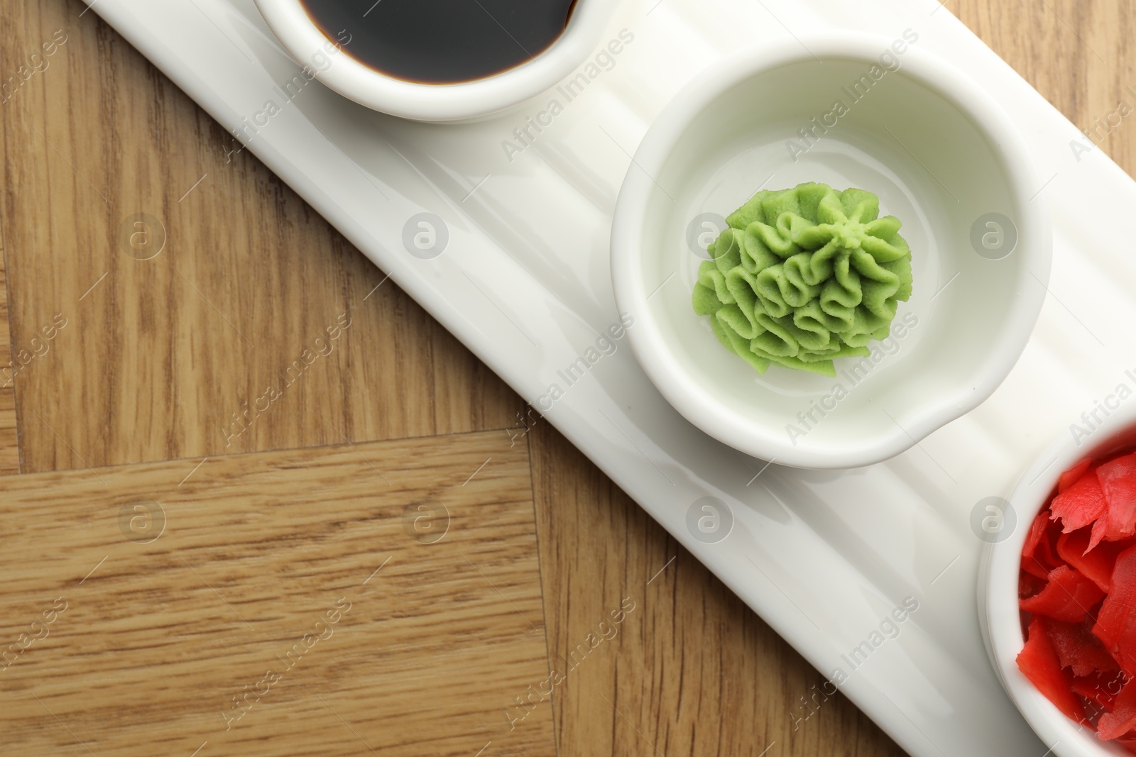 Photo of Hot wasabi paste, soy sauce and ginger on wooden table, top view