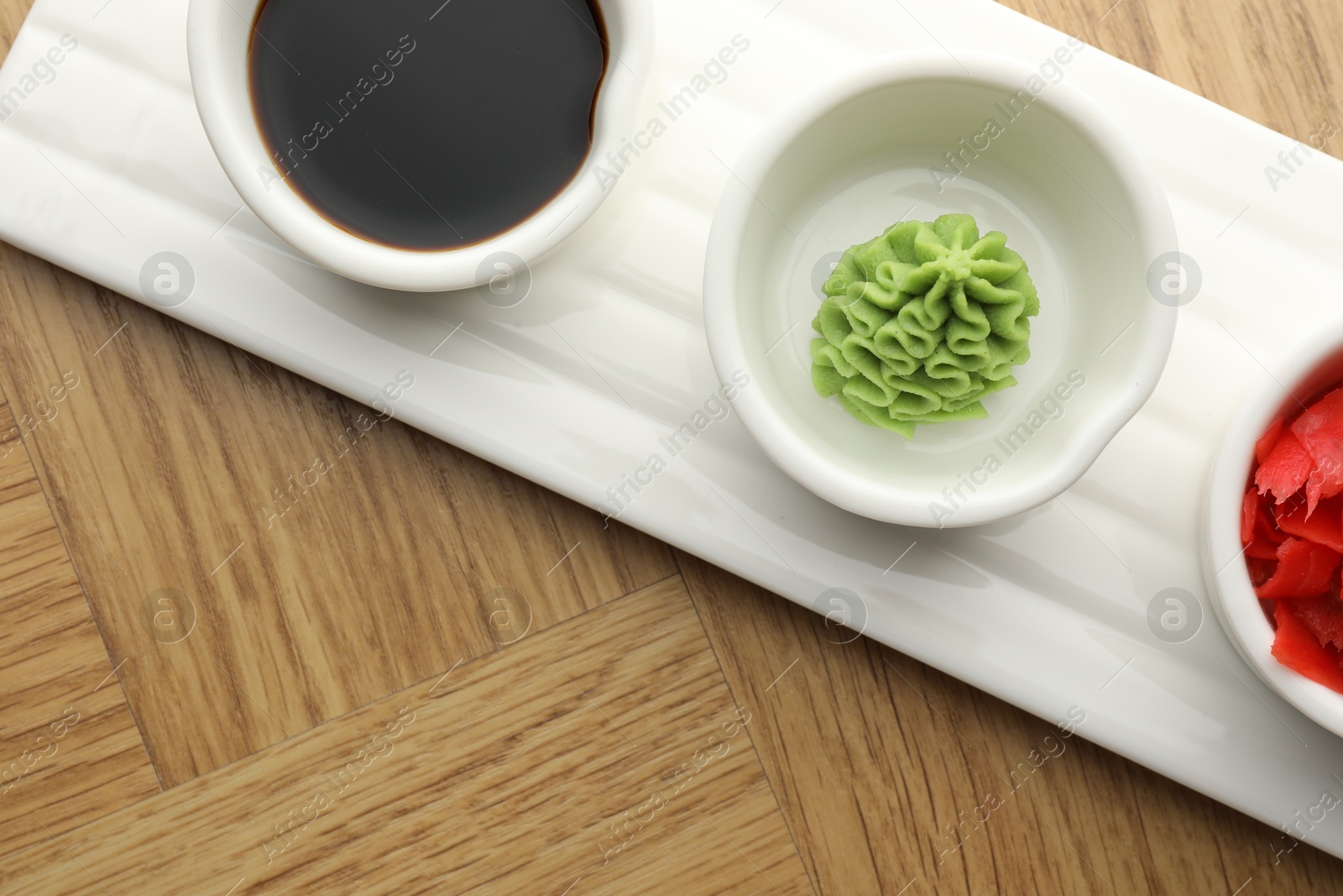 Photo of Hot wasabi paste, soy sauce and ginger on wooden table, top view