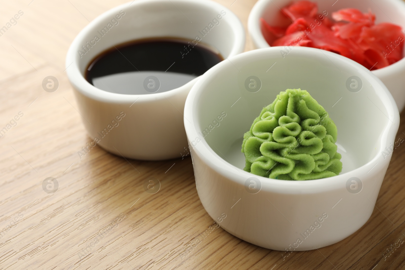 Photo of Hot wasabi paste, soy sauce and ginger on wooden table, closeup