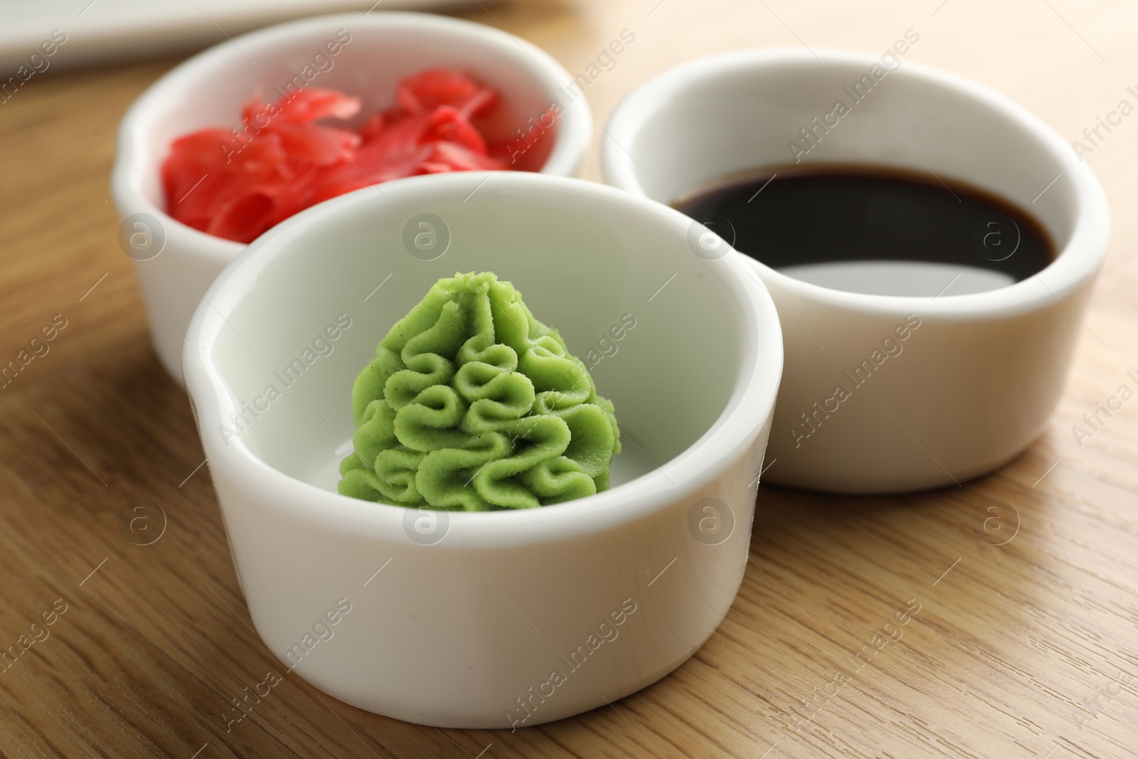 Photo of Hot wasabi paste, soy sauce and ginger on wooden table, closeup