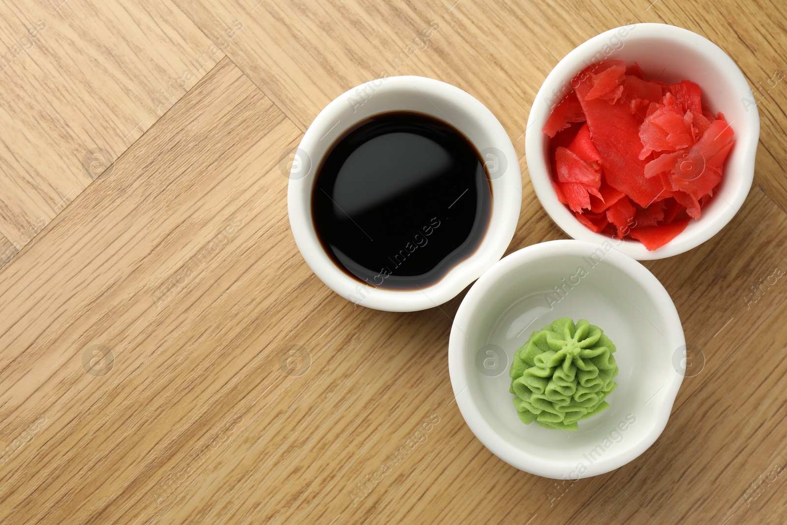 Photo of Hot wasabi paste, soy sauce and ginger on wooden table, flat lay. Space for text