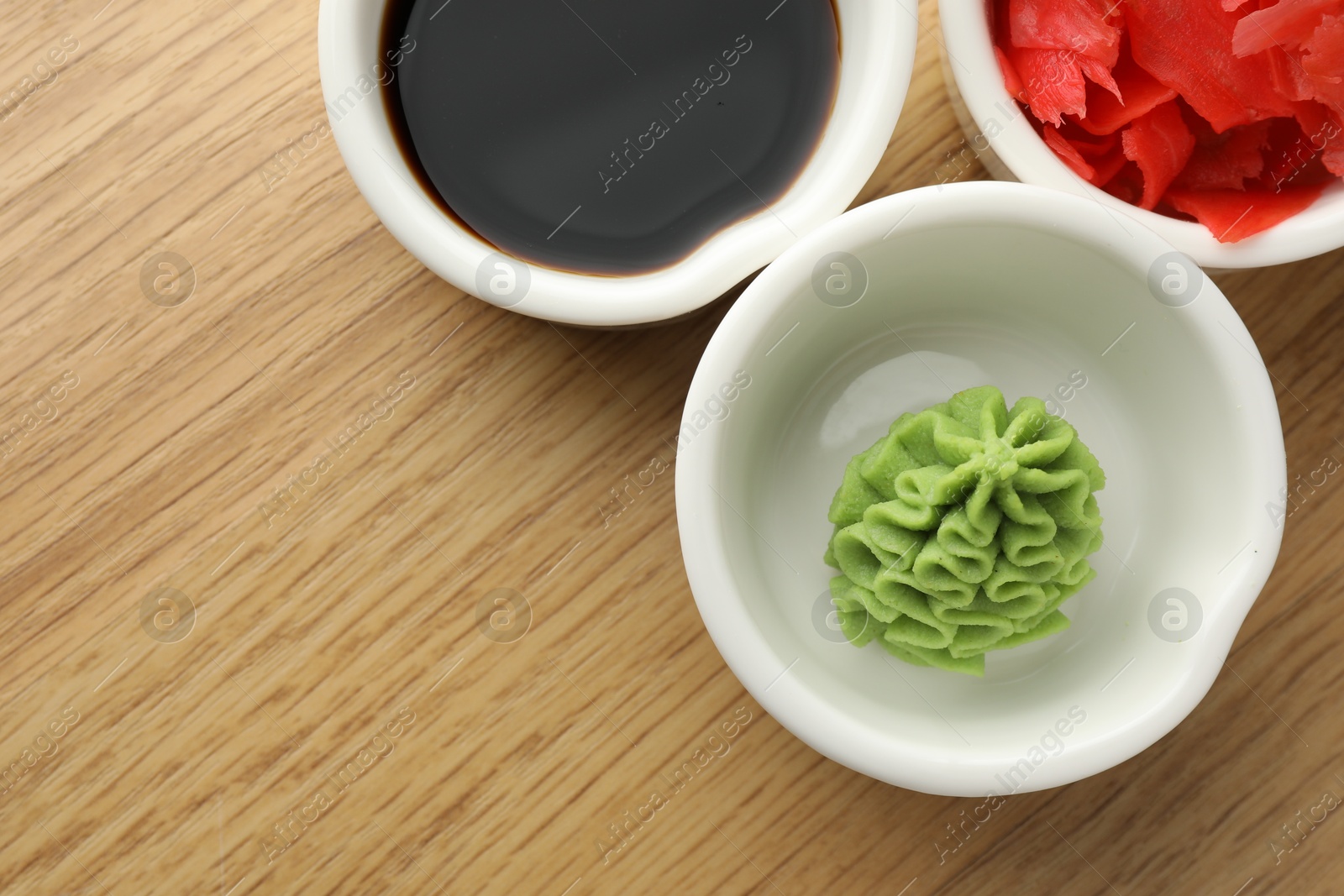 Photo of Hot wasabi paste, soy sauce and ginger on wooden table, flat lay. Space for text