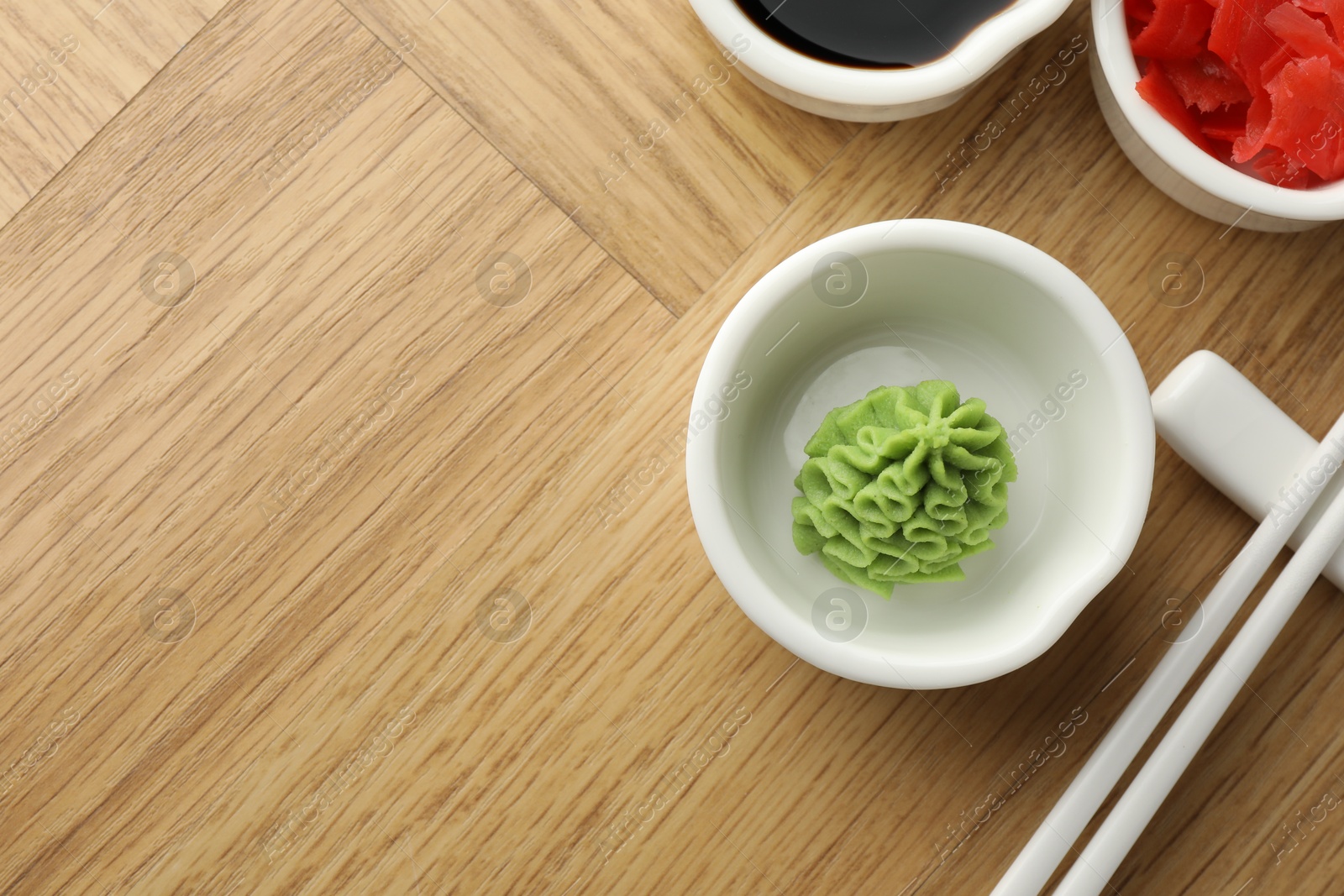 Photo of Hot wasabi paste, soy sauce, ginger and chopsticks on wooden table, flat lay. Space for text