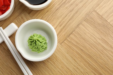 Photo of Hot wasabi paste, soy sauce, ginger and chopsticks on wooden table, flat lay. Space for text