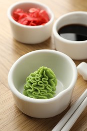 Photo of Hot wasabi paste, soy sauce, ginger and chopsticks on wooden table, closeup